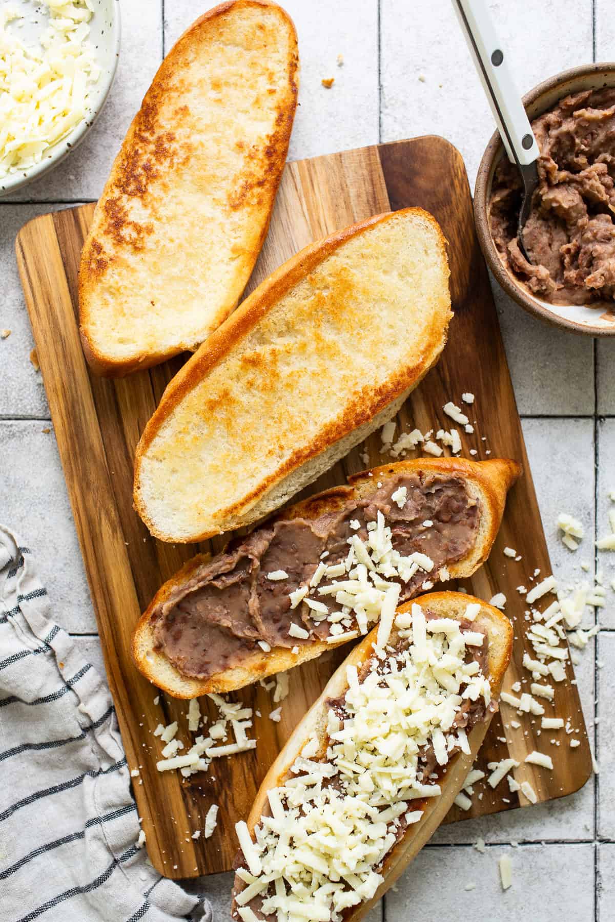 Refried beans and shredded cheese spread on bolillo bread halves.