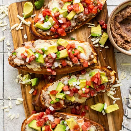 Traditional Mexican molletes topped with refried beans, cheese, pico de gallo, and avocado.