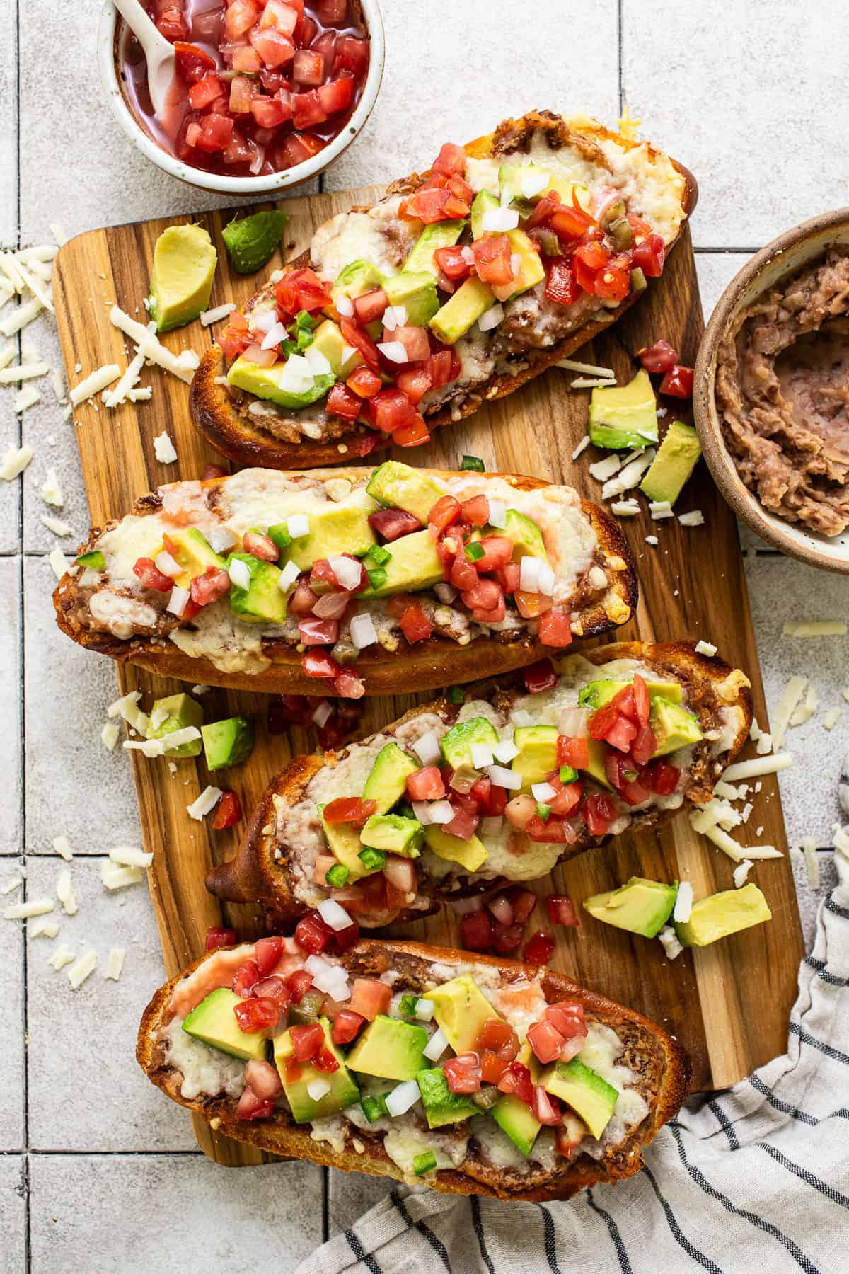 Molletes topped with refried beans, cheese, pico de gallo, and avocado.