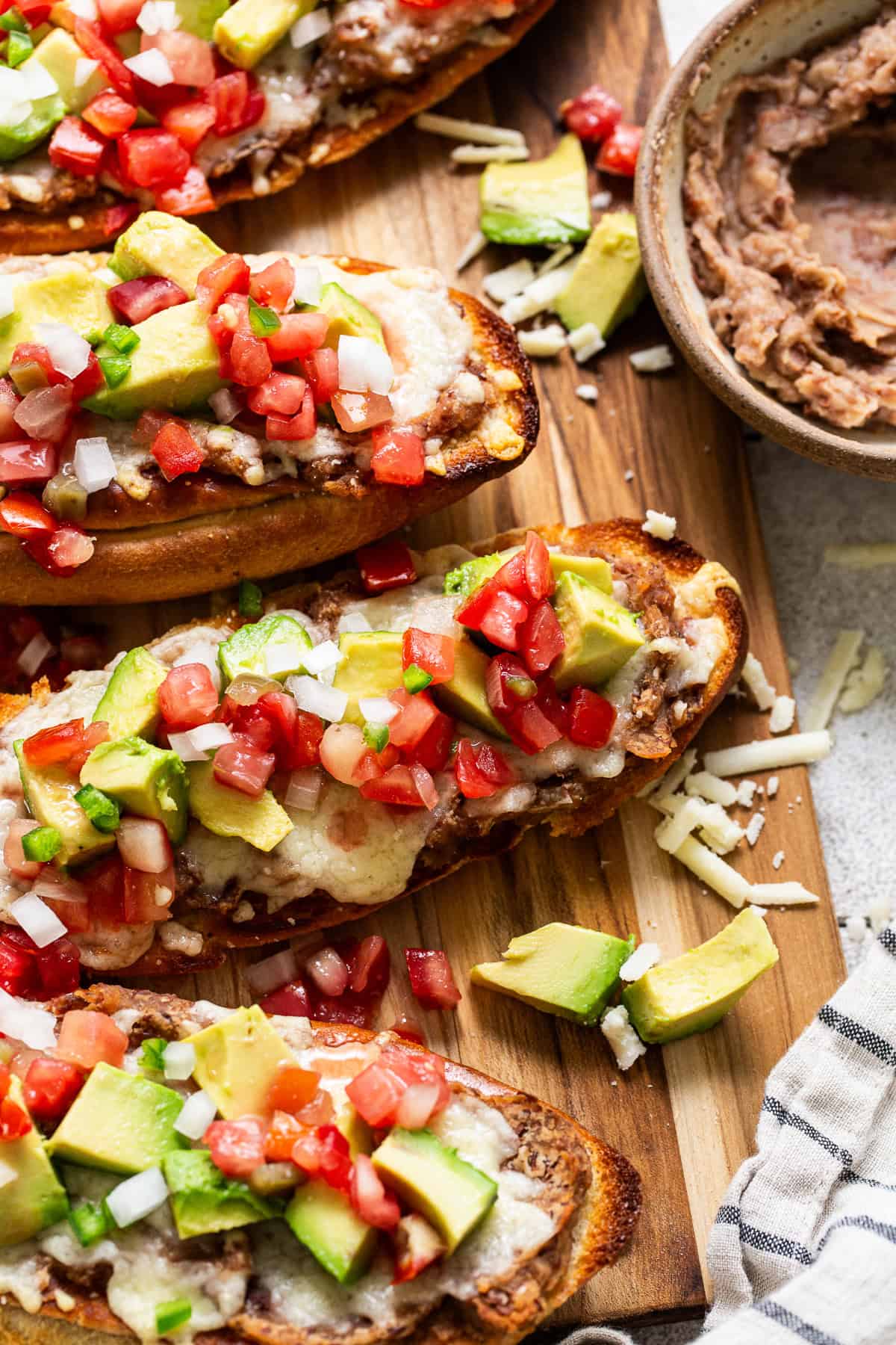 Molletes topped with refried beans, cheese, pico de gallo, and avocado.