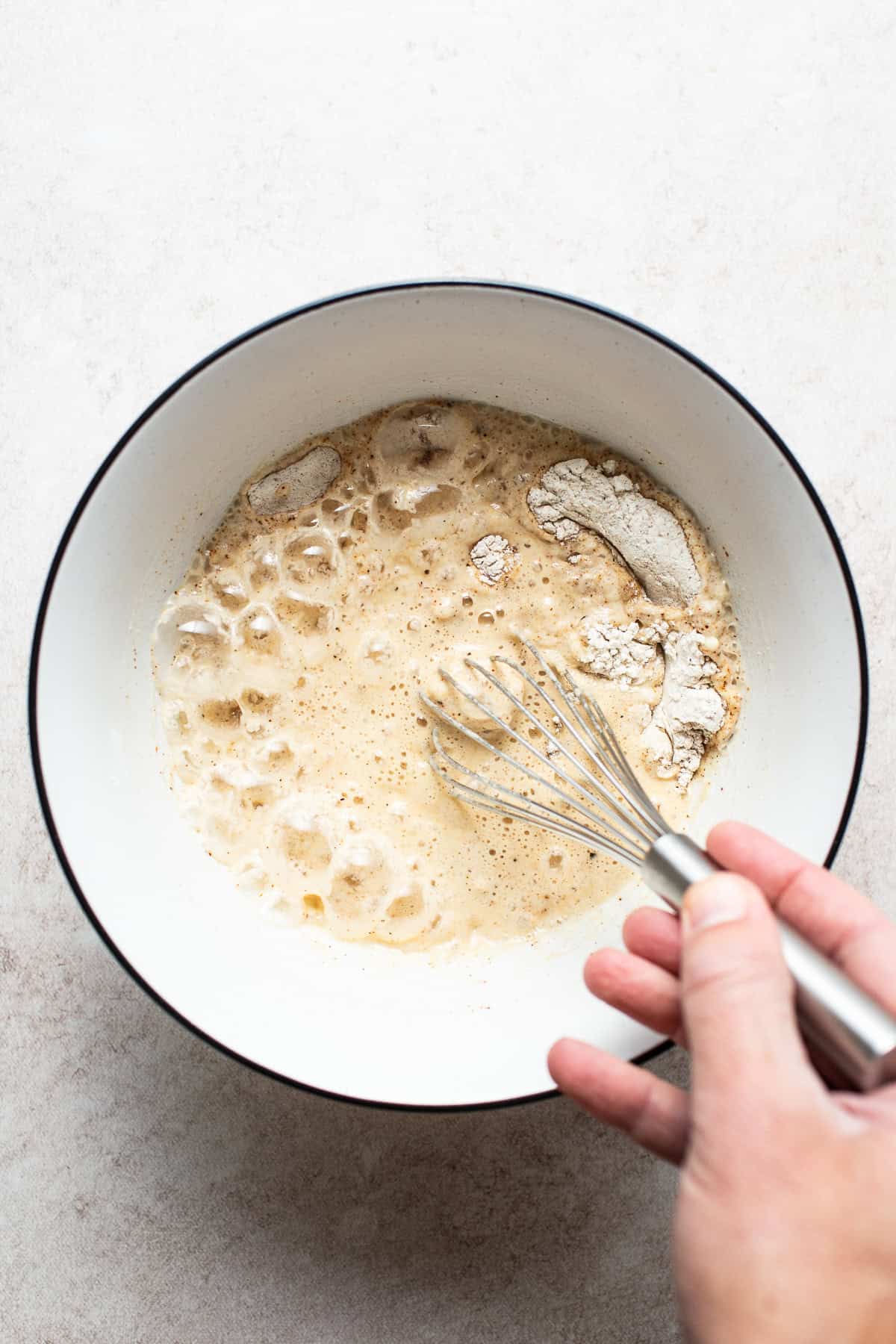 Flour., seasonings, and beer being whisked together in a bowl.