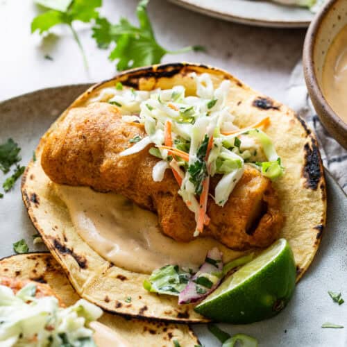 Baja fish tacos served with chipotle lime crema and topped with a creamy cabbage slaw on a plate