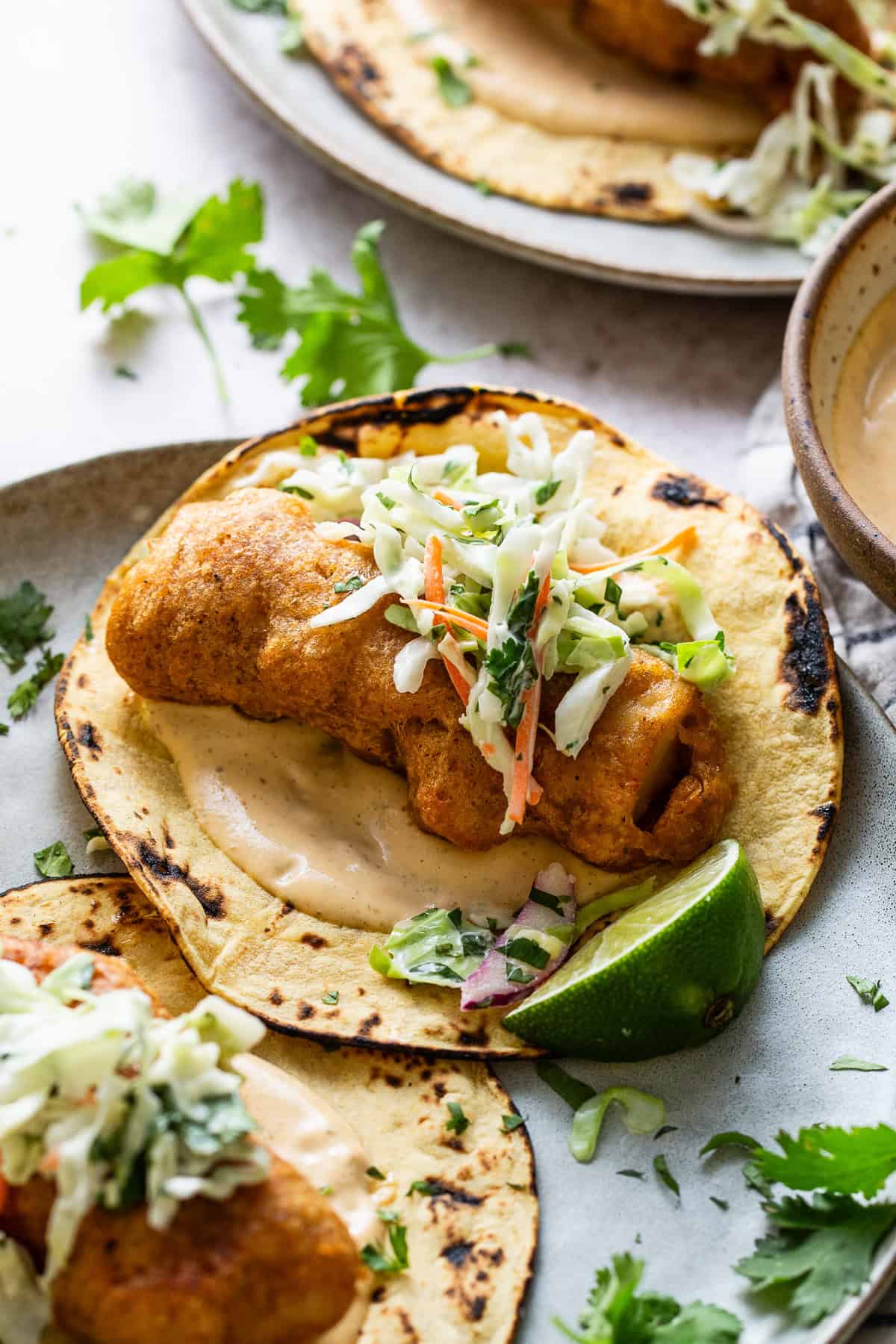 Baja fish tacos served with chipotle lime crema and topped with a creamy cabbage slaw on a plate