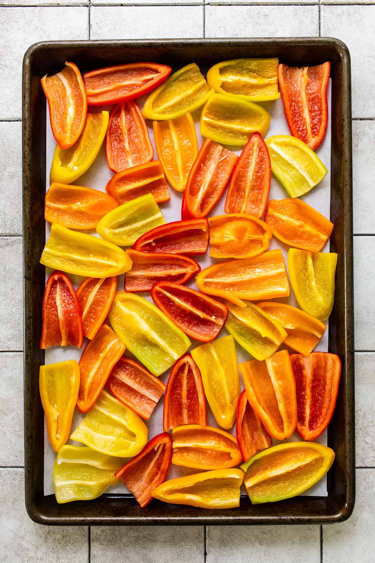 Mini bell peppers sliced in half lengthwise on a sheet pan in a single layer.