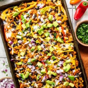 Bell pepper nachos on a sheet pan topped with avocado, onion, cilantro, and other nacho toppings.