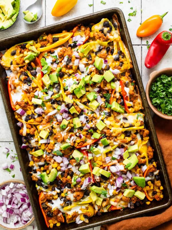 Bell pepper nachos on a sheet pan topped with avocado, onion, cilantro, and other nacho toppings.