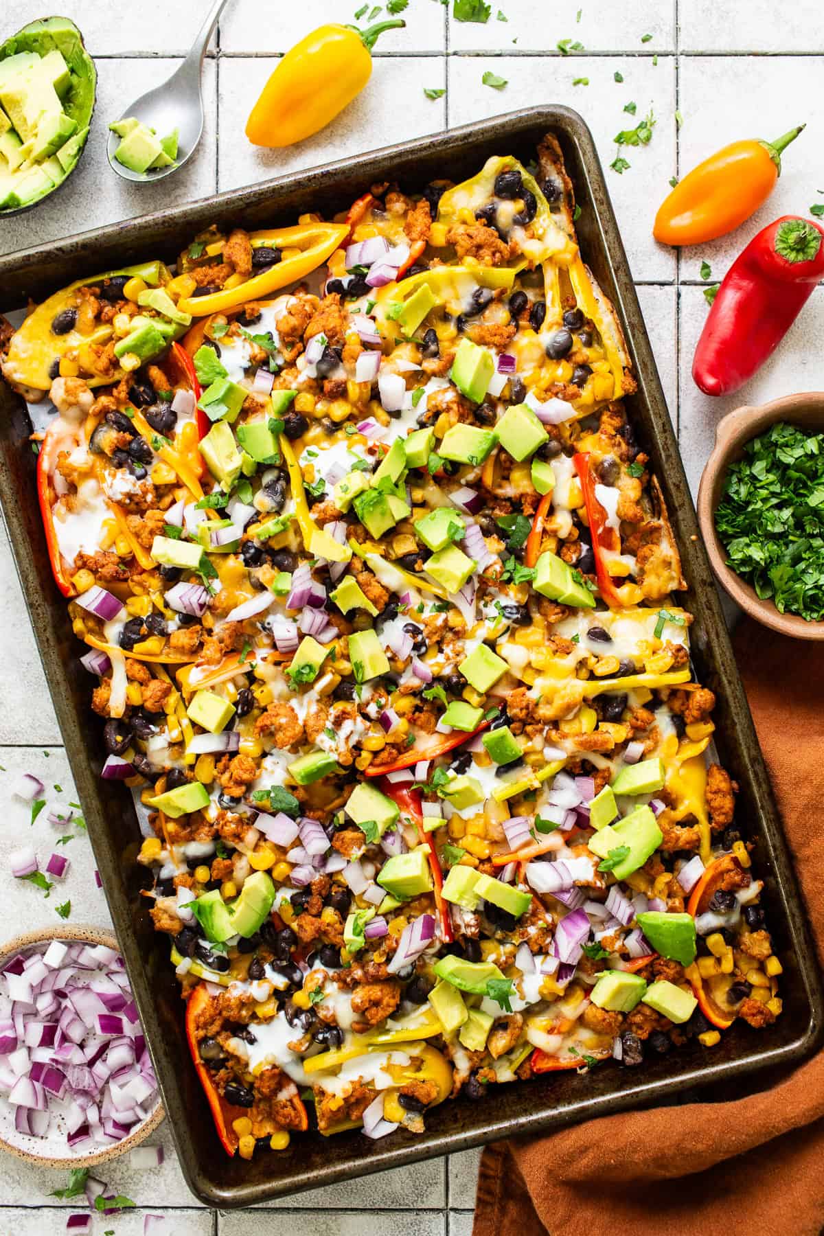 Bell pepper nachos on a sheet pan topped with avocado, onion, cilantro, and other nacho toppings.