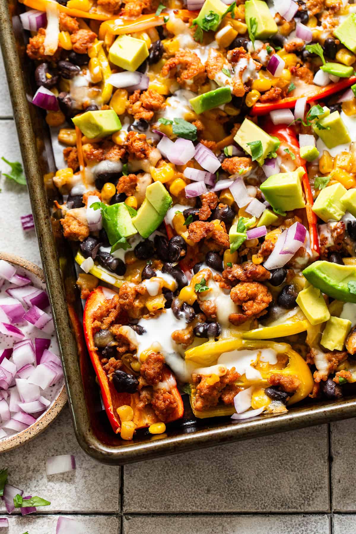 Bell pepper nachos on a sheet pan ready to serve with diced avocado, onion, sour cream, and the best nacho toppings.