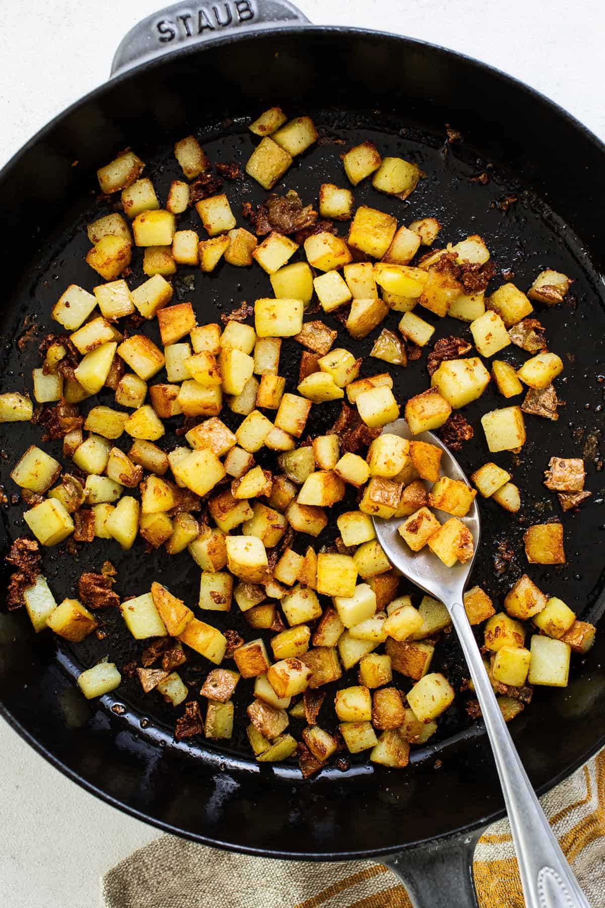 Diced potatoes and chorizo cooking in a large skillet with olive oil.