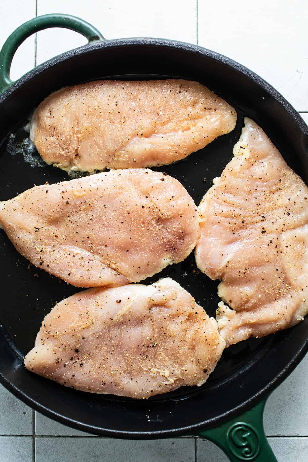 Chicken breast cooking in a cast iron skillet seasoned with salt and black pepper.