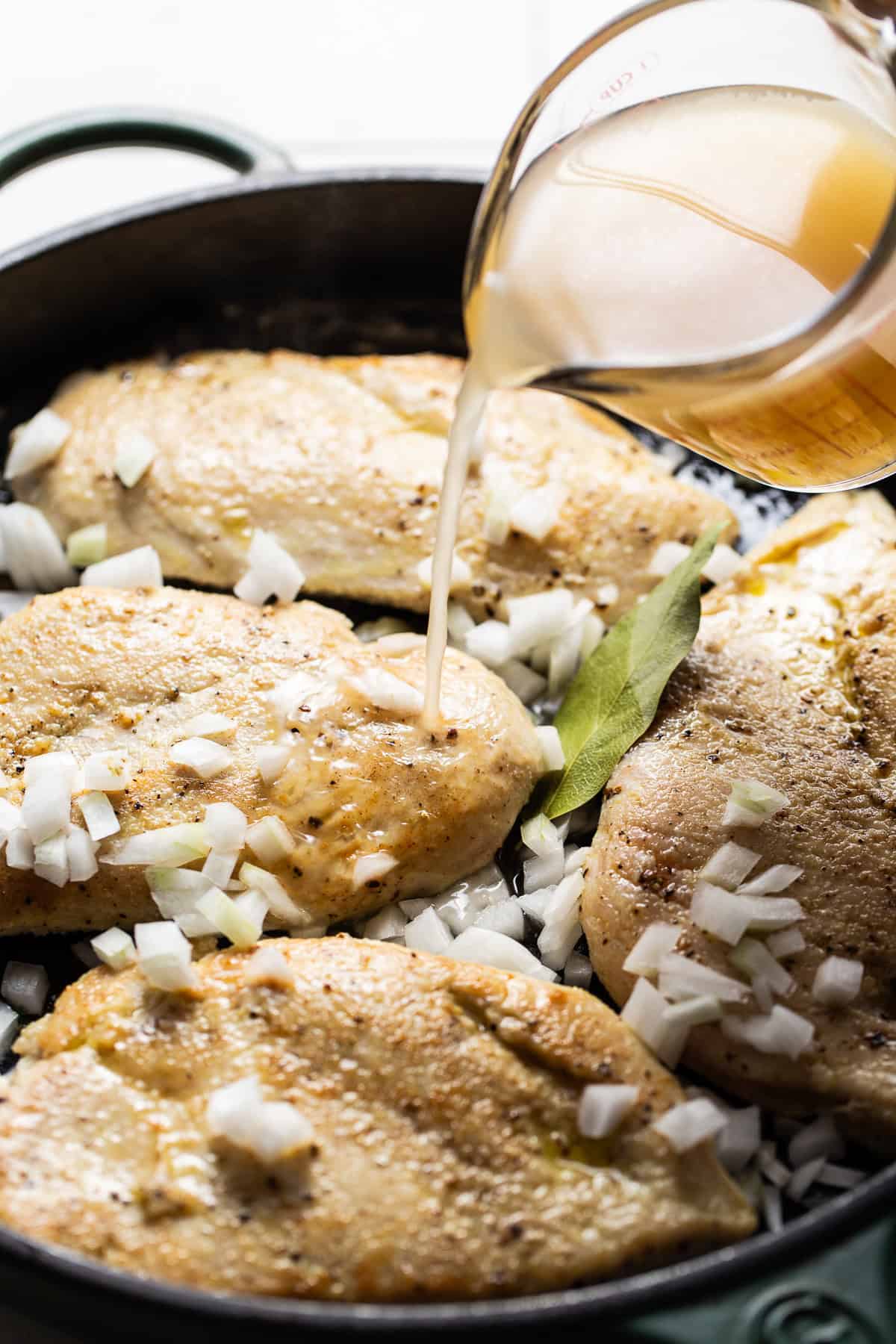 Broth being poured into a skillet with seared chicken breast to make shredded chicken.