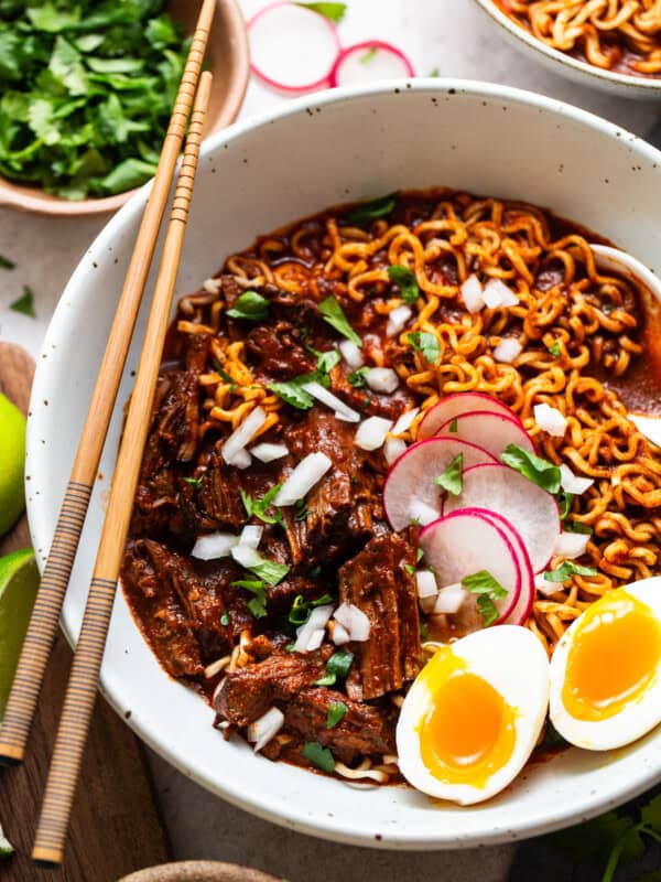 Birra ramen in a bowl topped with cilantro, onion, and radishes and served with a soft boiled egg.