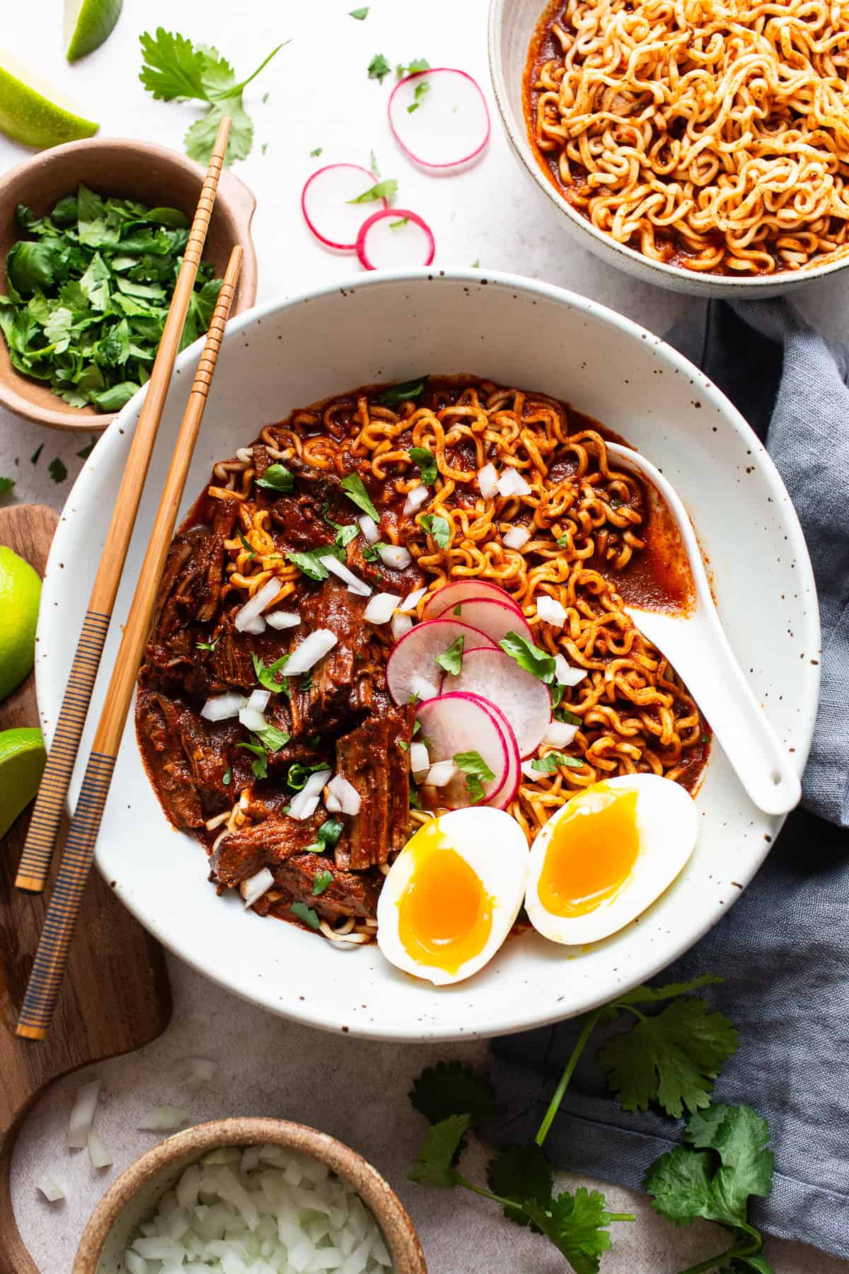 A bowl of birria ramen topped with diced onion, cilantro, and radishes ready to enjoy.