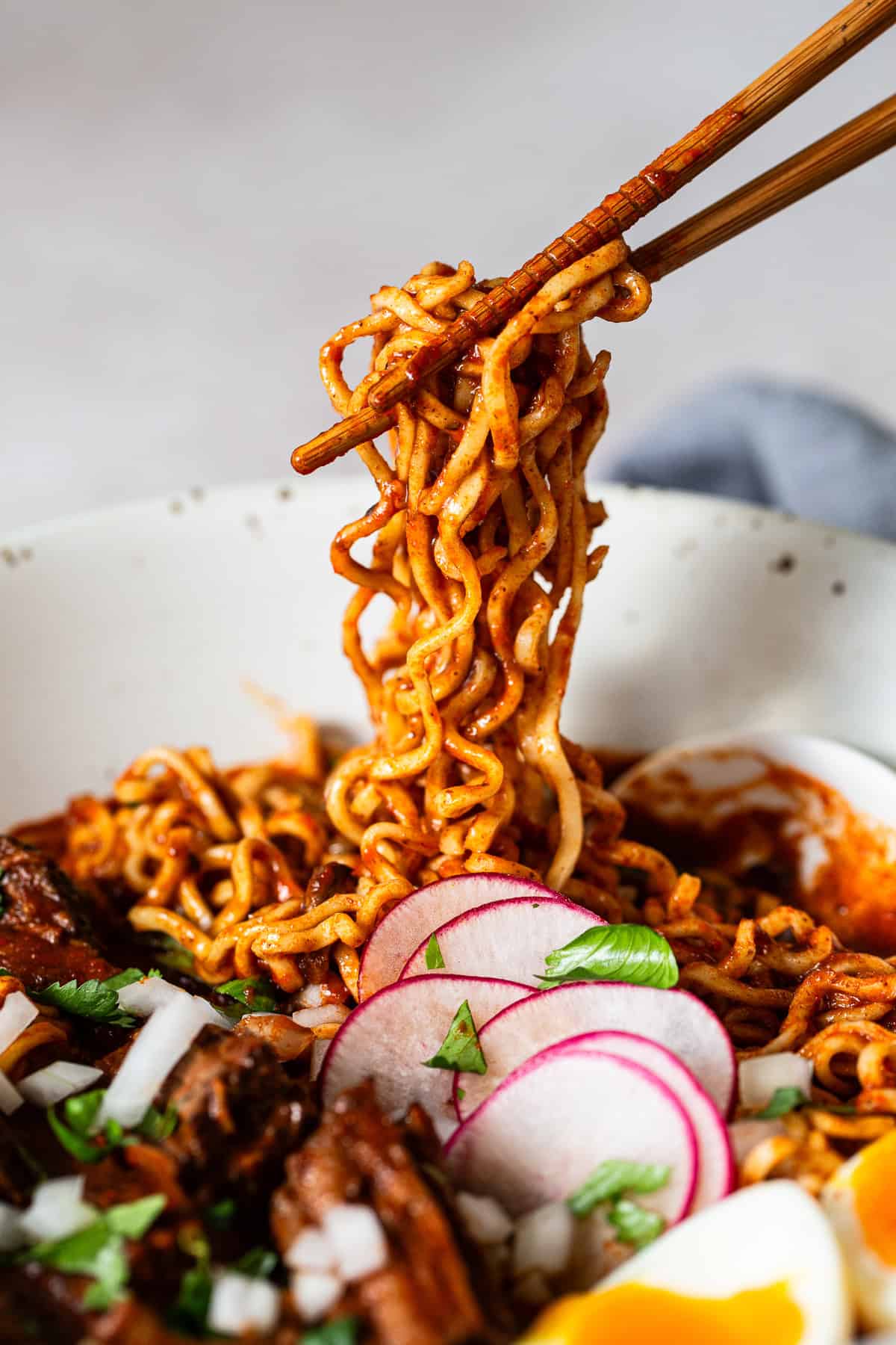 Birria ramen noodles being pulled up out of the bowl with chopsticks.