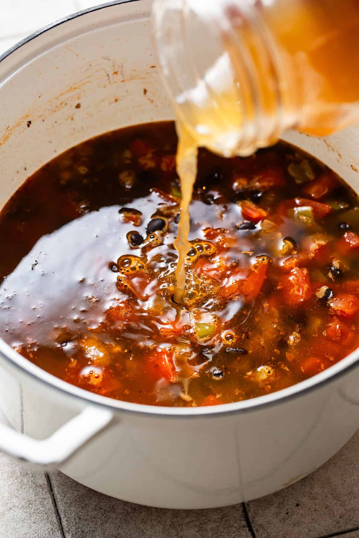 Vegetable broth being poured into a pot of black bean soup.