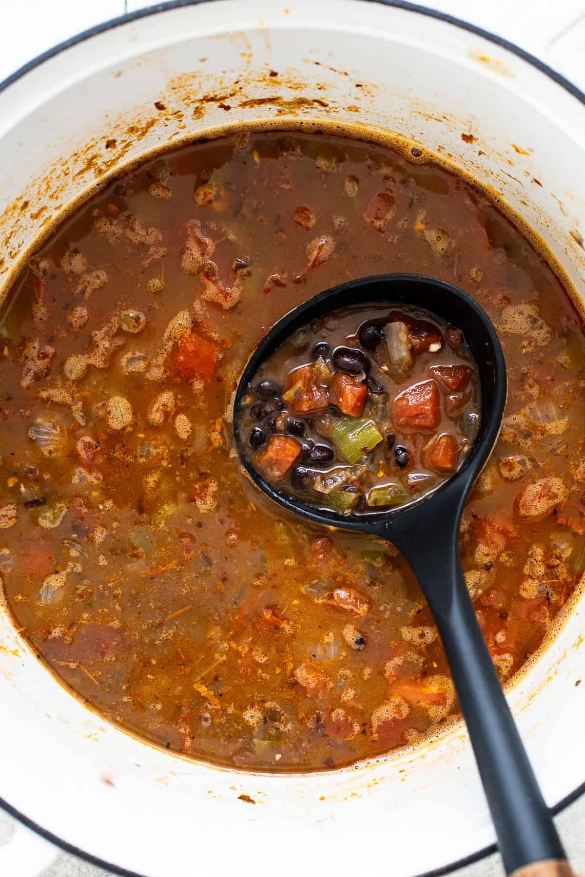 A ladle with black bean soup in a pot ready to be served.