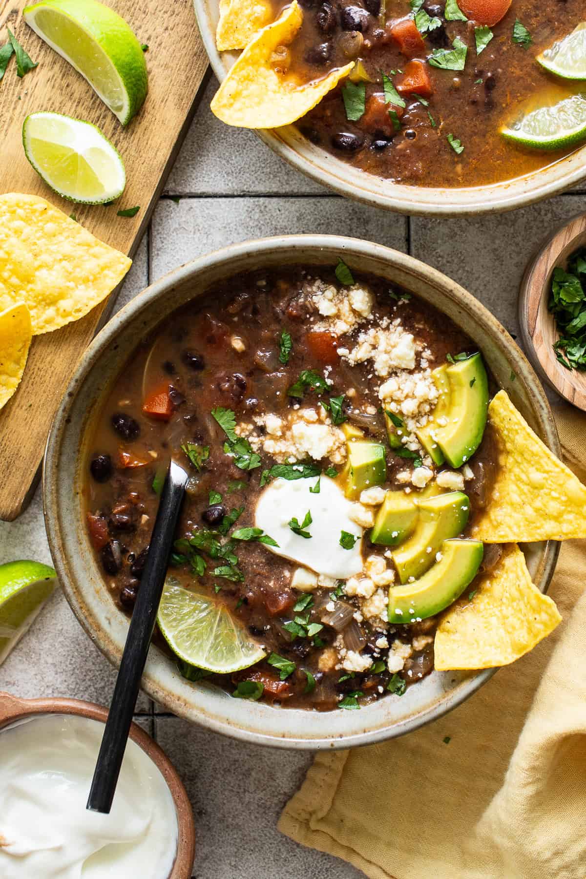 A bowl of black bean soup topped with sour cream, avocados, and cilantro.