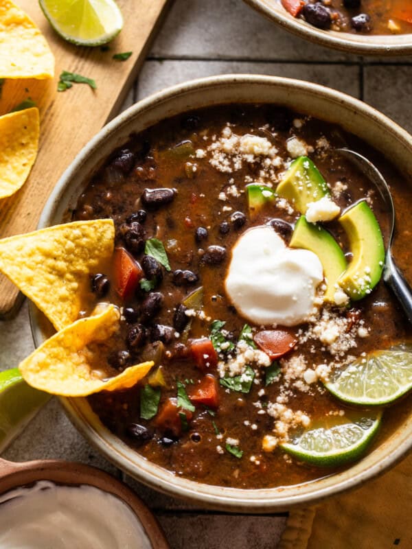 Vegetarian black bean soup in a bowl topped with avocados, cilantro, and limes.