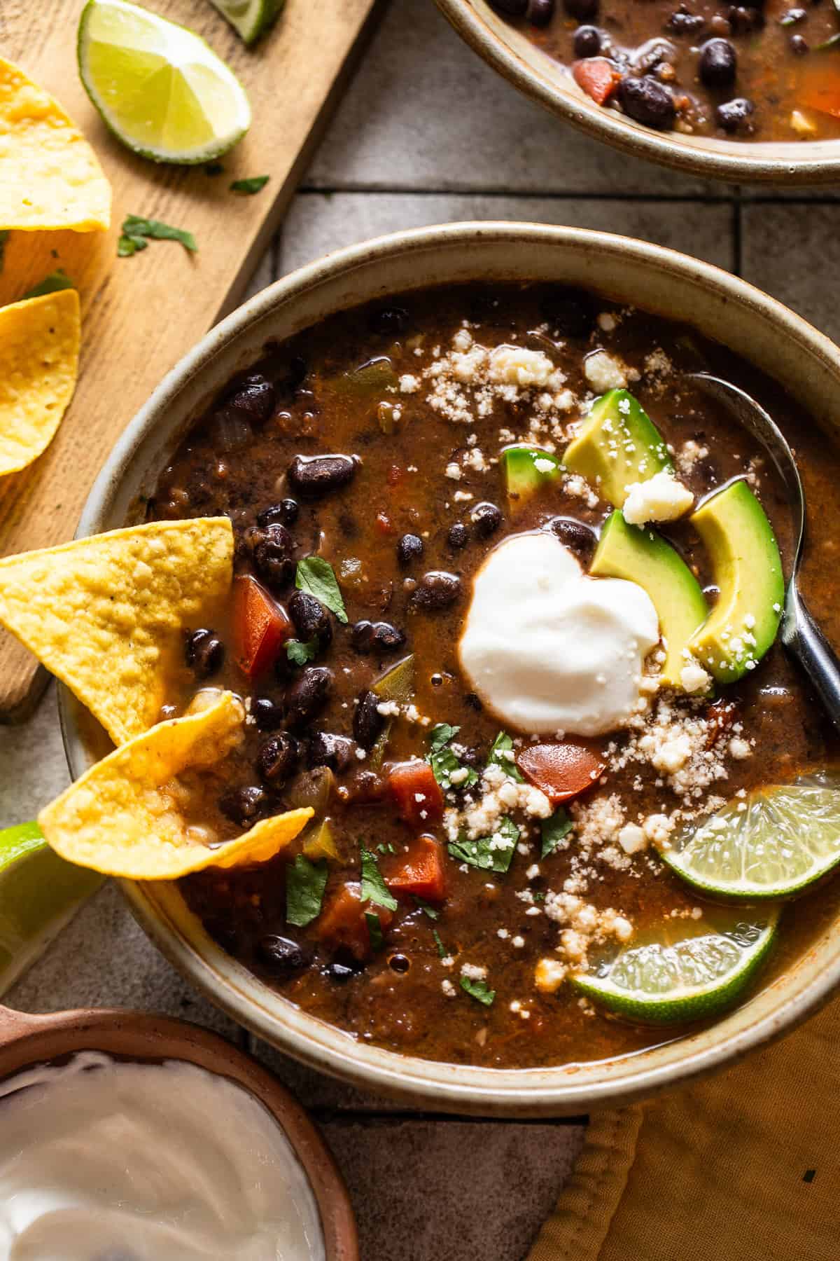 Vegetarian black bean soup in a bowl topped with avocados, cilantro, and limes.