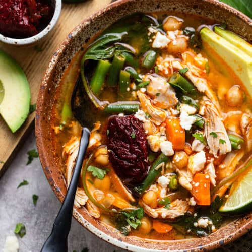 Caldo Tlalpeño garnished with a chipotle pepper in adobo sauce, queso fresco, and cilantro.