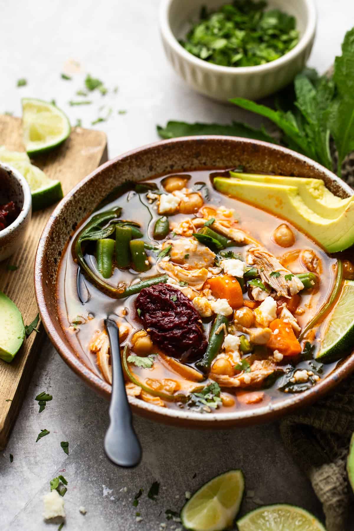 Caldo Tlalpeño on a table with fresh lime wedges and cilantro.