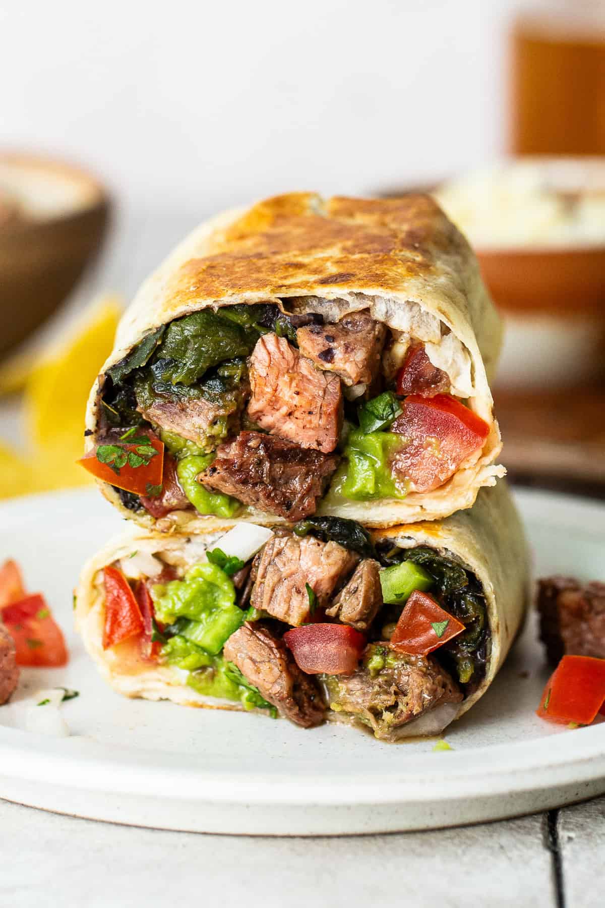 Carne asada burrito cut in half and stacked on a plate.