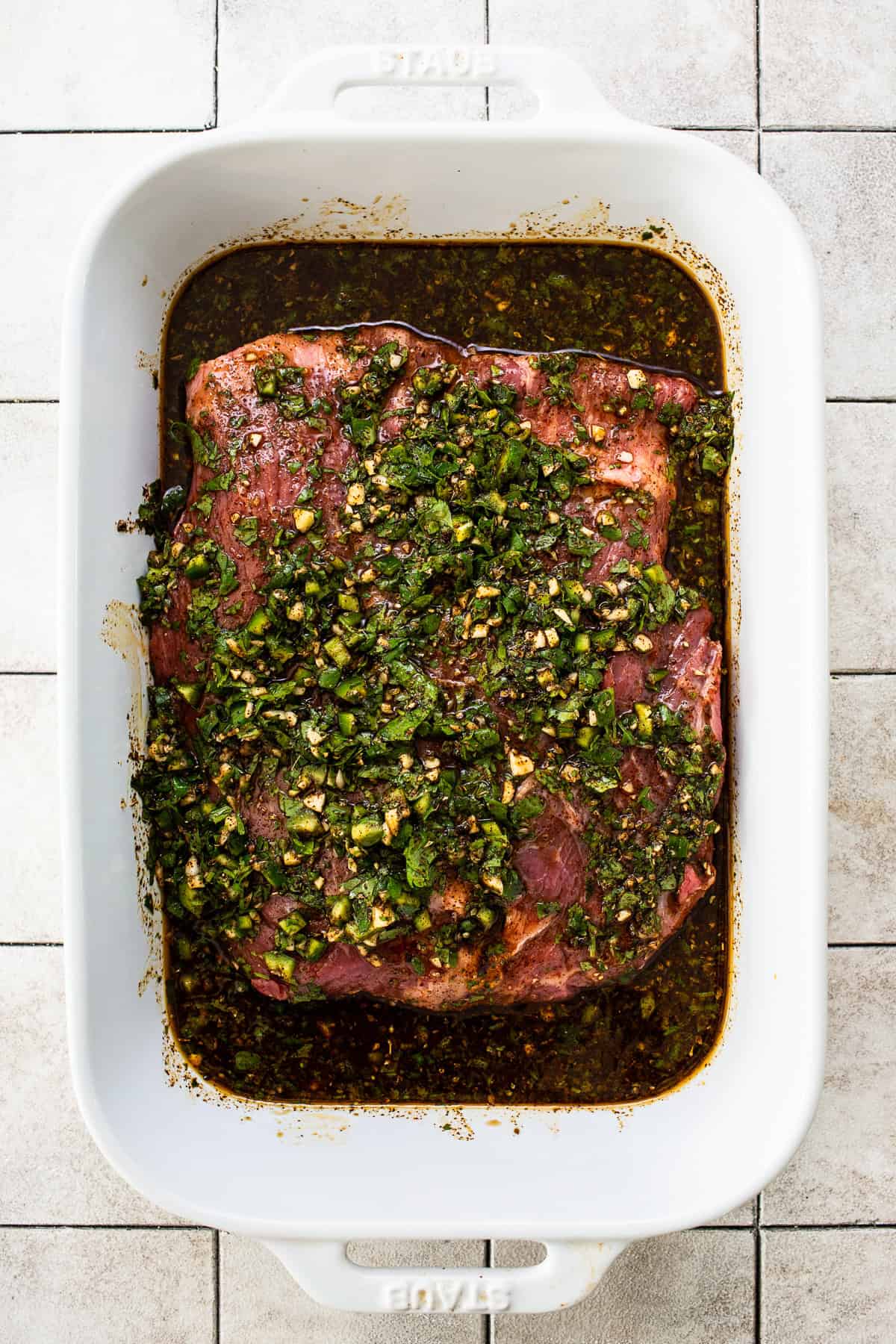 Flank steak in a baking dish covered with a carne asada marinade.