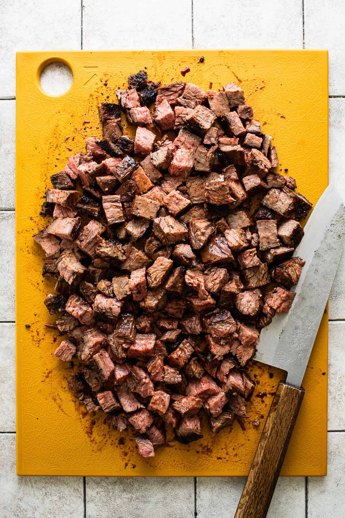 Cooked carne asada steak cut into bite-sized pieces on a cutting board.