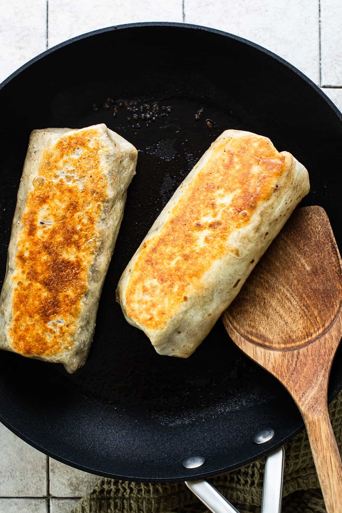 Toasted carne asada burritos in a skillet. 