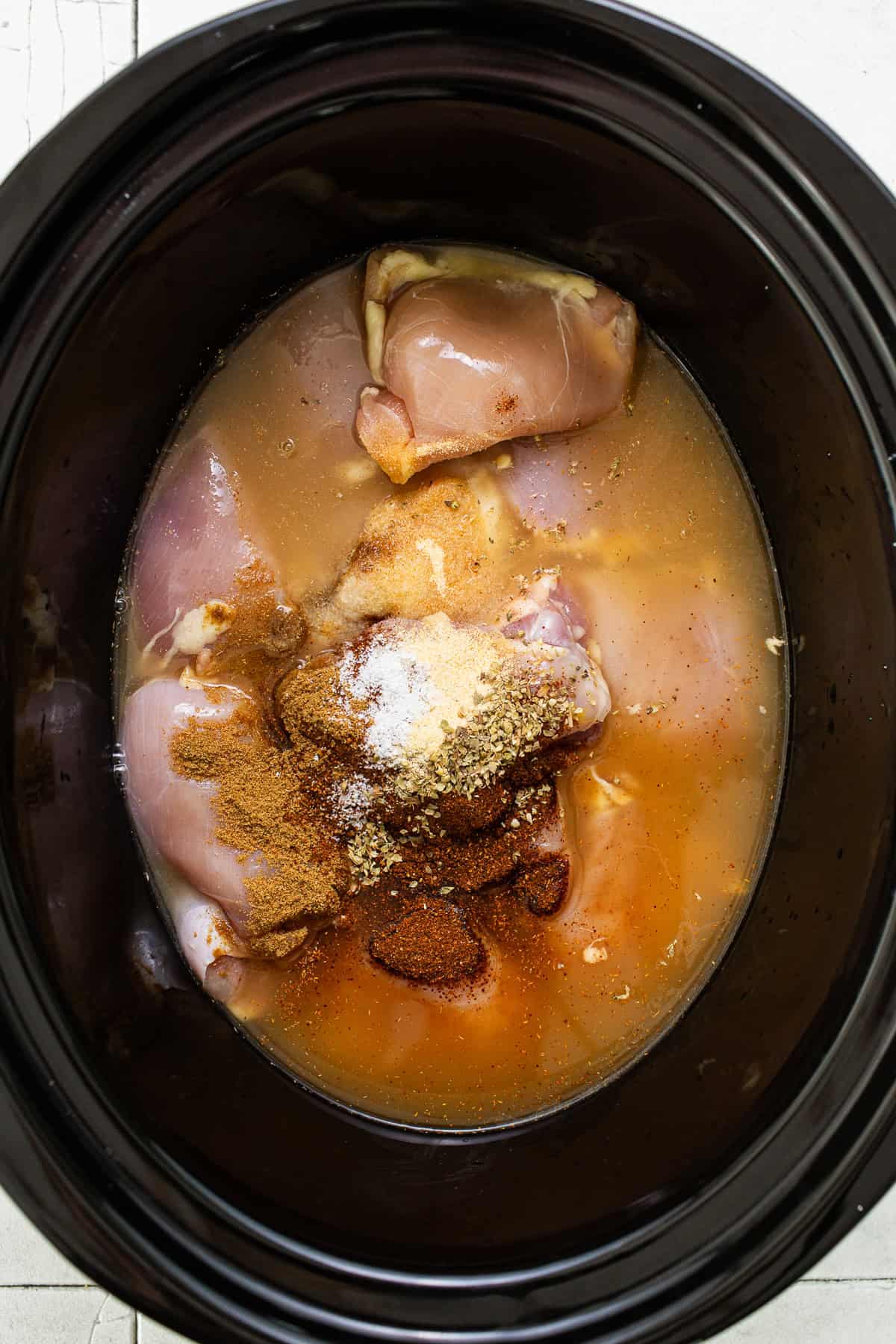 A crockpot filled with chicken and seasonings to make chicken carnitas.