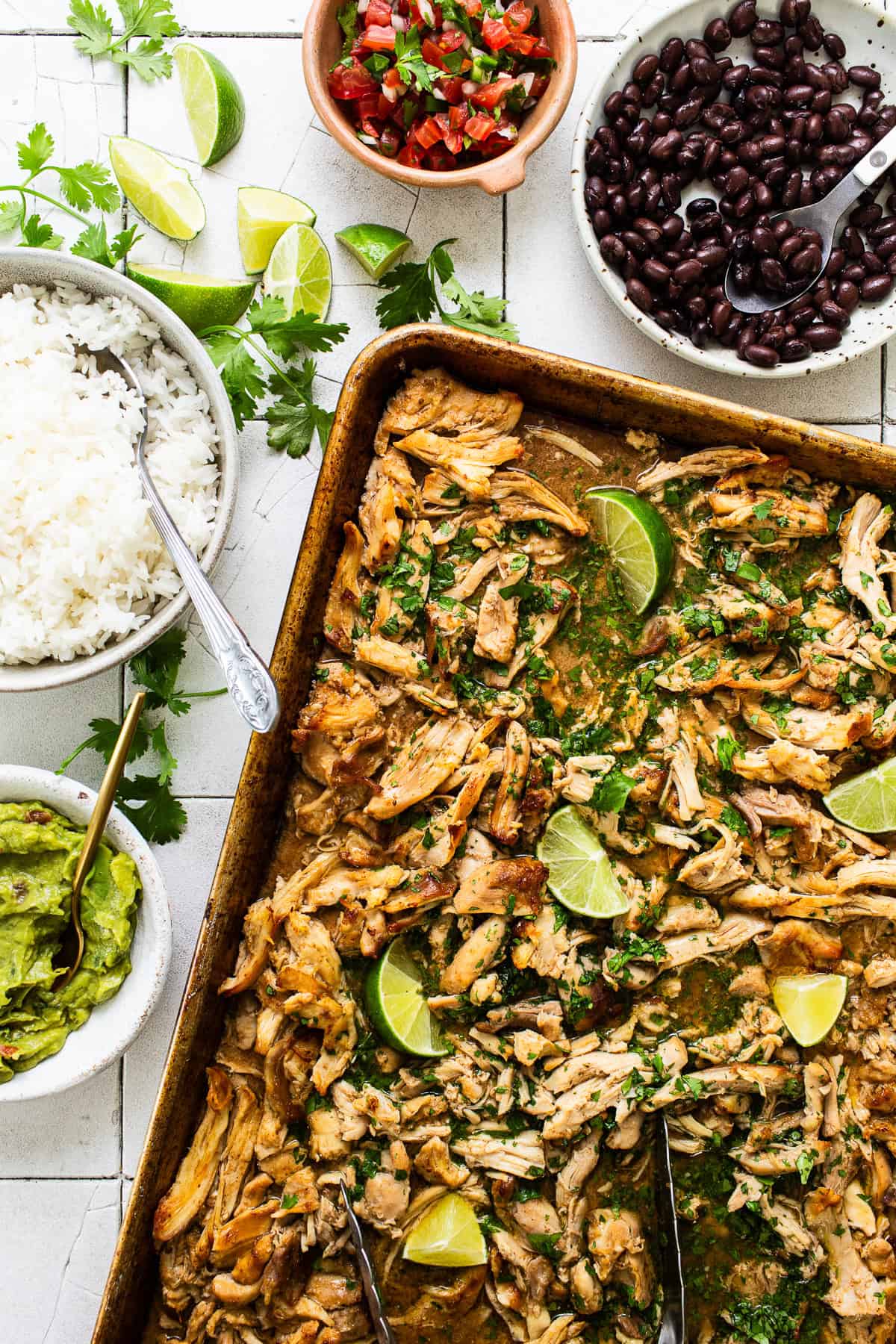 Chicken carnitas on a baking sheet with toppings on the side ready to eat. 