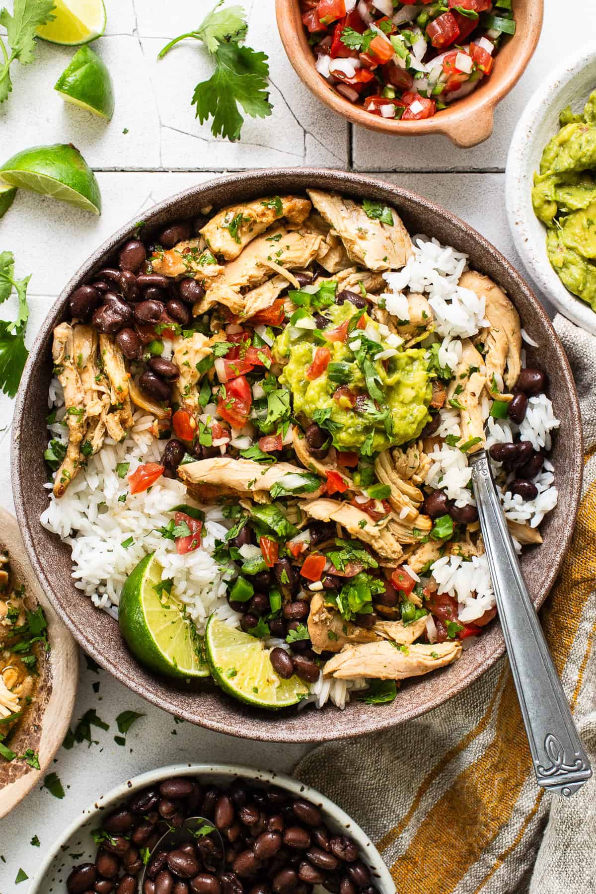 A bowl of rice with chicken carnitas, guacamole, pico de gallo, cilantro, and lime.