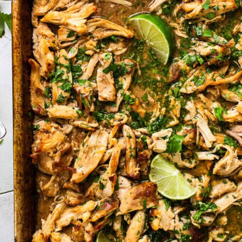 Chicken carnitas on a sheet pan with caramelized crispy edges and garnished with cilantro and fresh lime juice.