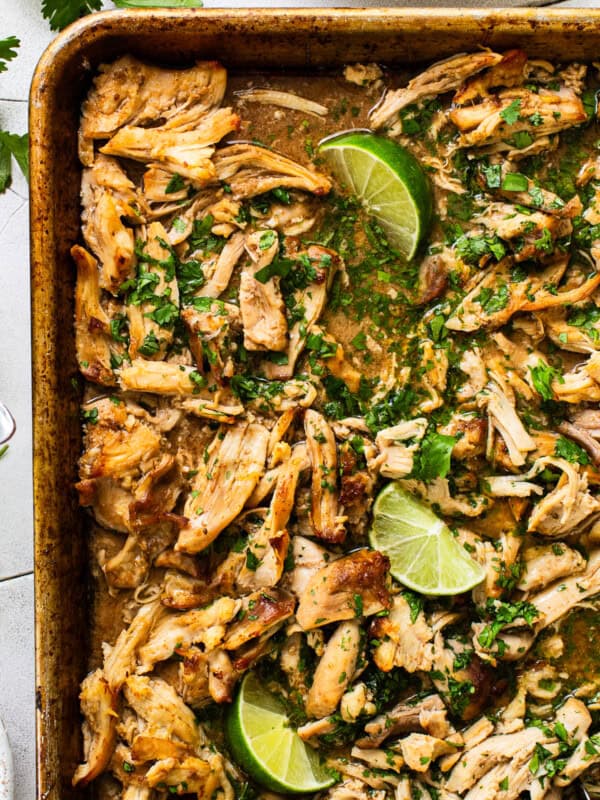 Chicken carnitas on a sheet pan with caramelized crispy edges and garnished with cilantro and fresh lime juice.