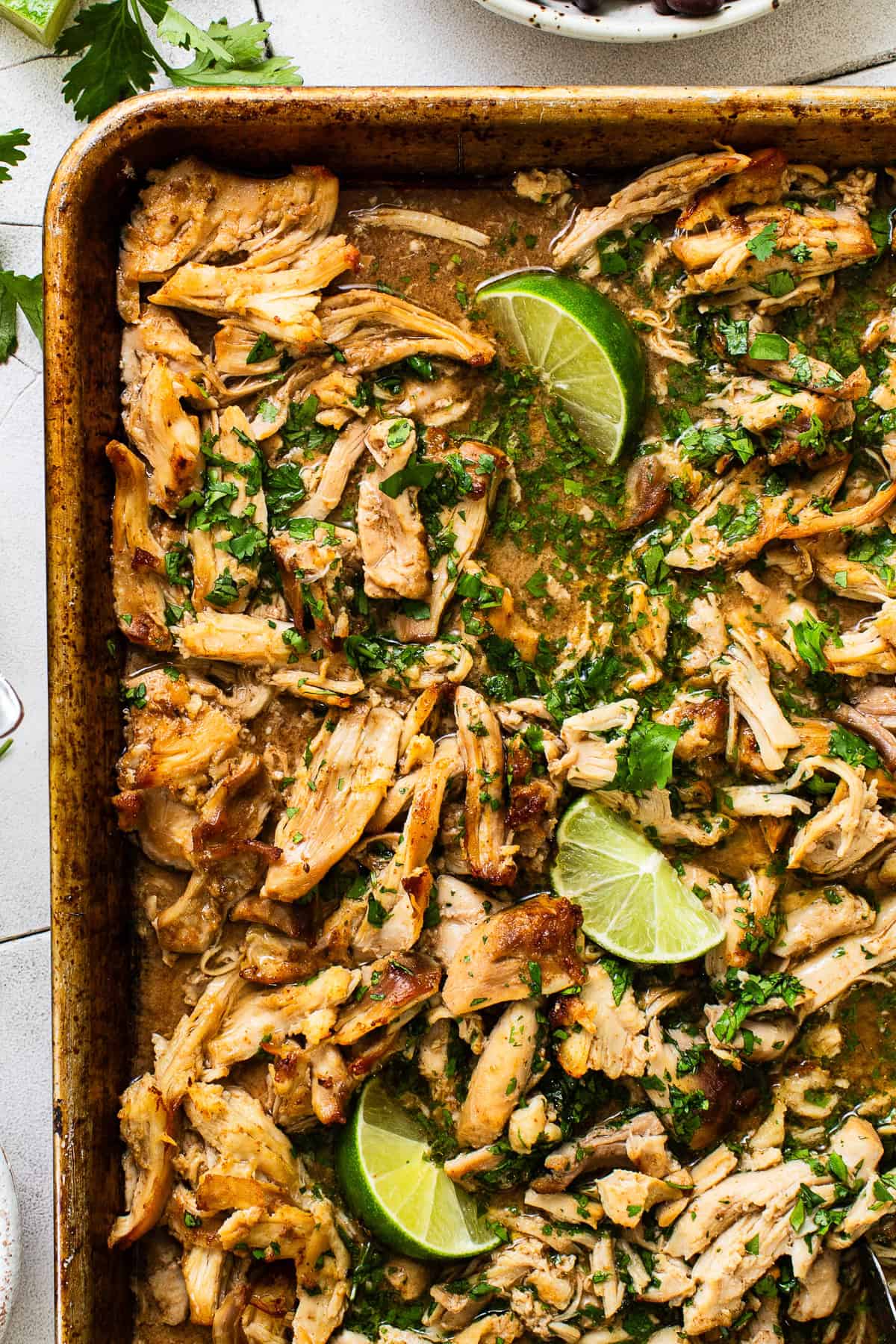 Baking sheet with chicken carnitas topped with cilantro and limes. 