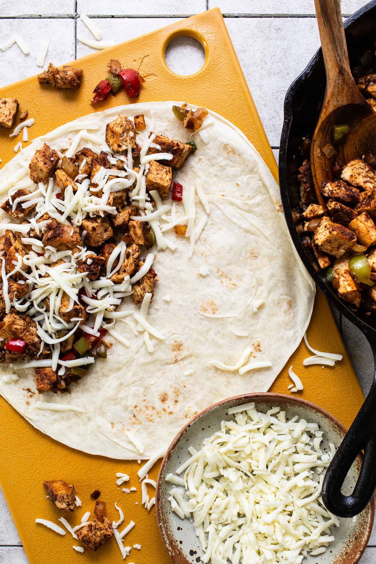 Tortilla being filled with chicken fajitas and covered with cheese.