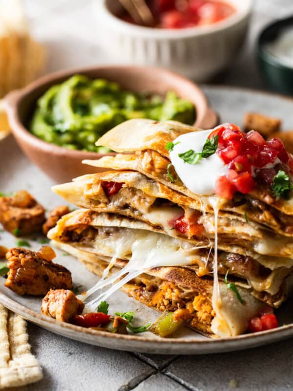 Chicken fajita quesadillas stacked on a plate with sour cream, lettuce, and tomatoes on top.