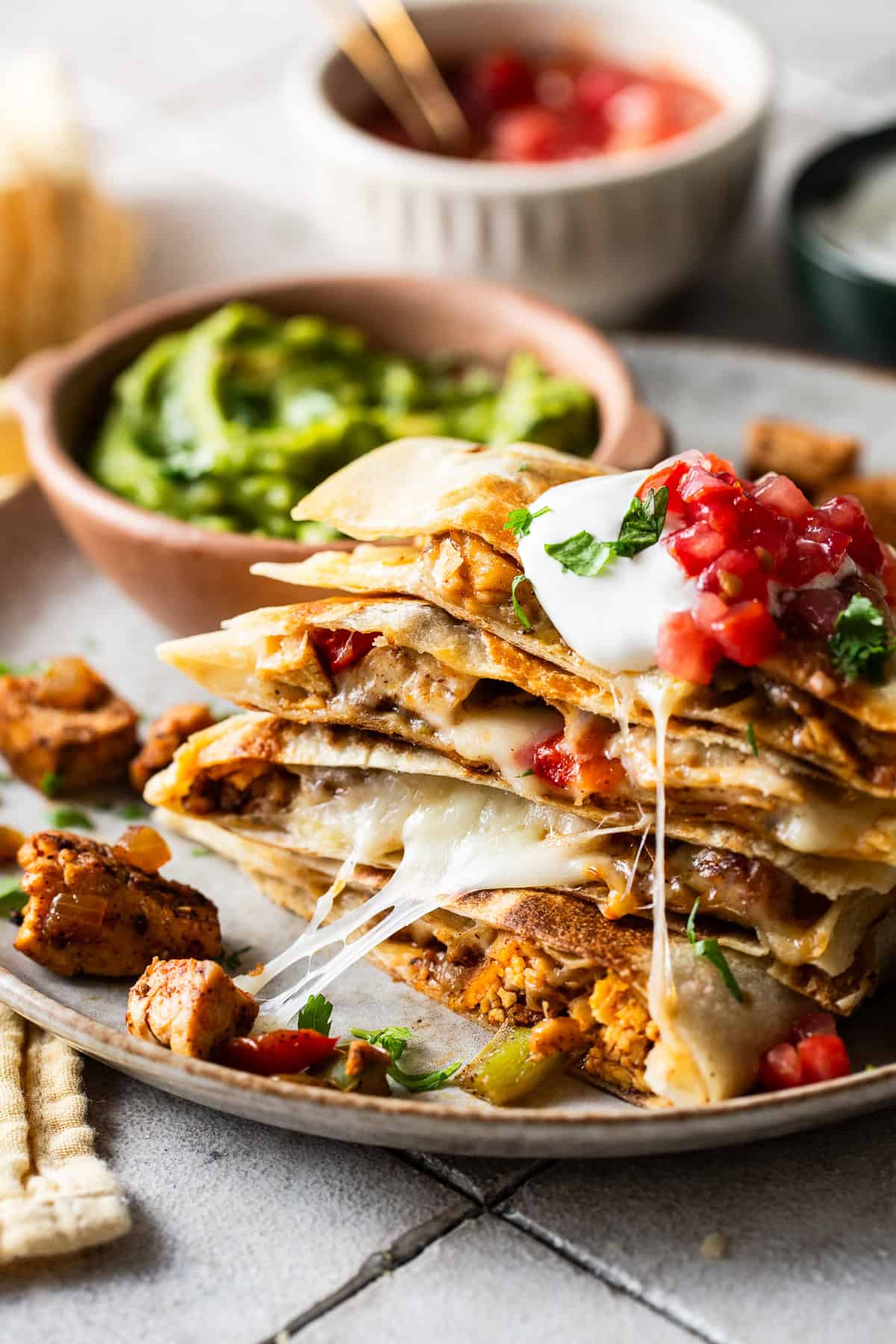 Chicken fajita quesadillas stacked on a plate with sour cream, lettuce, and tomatoes on top. 