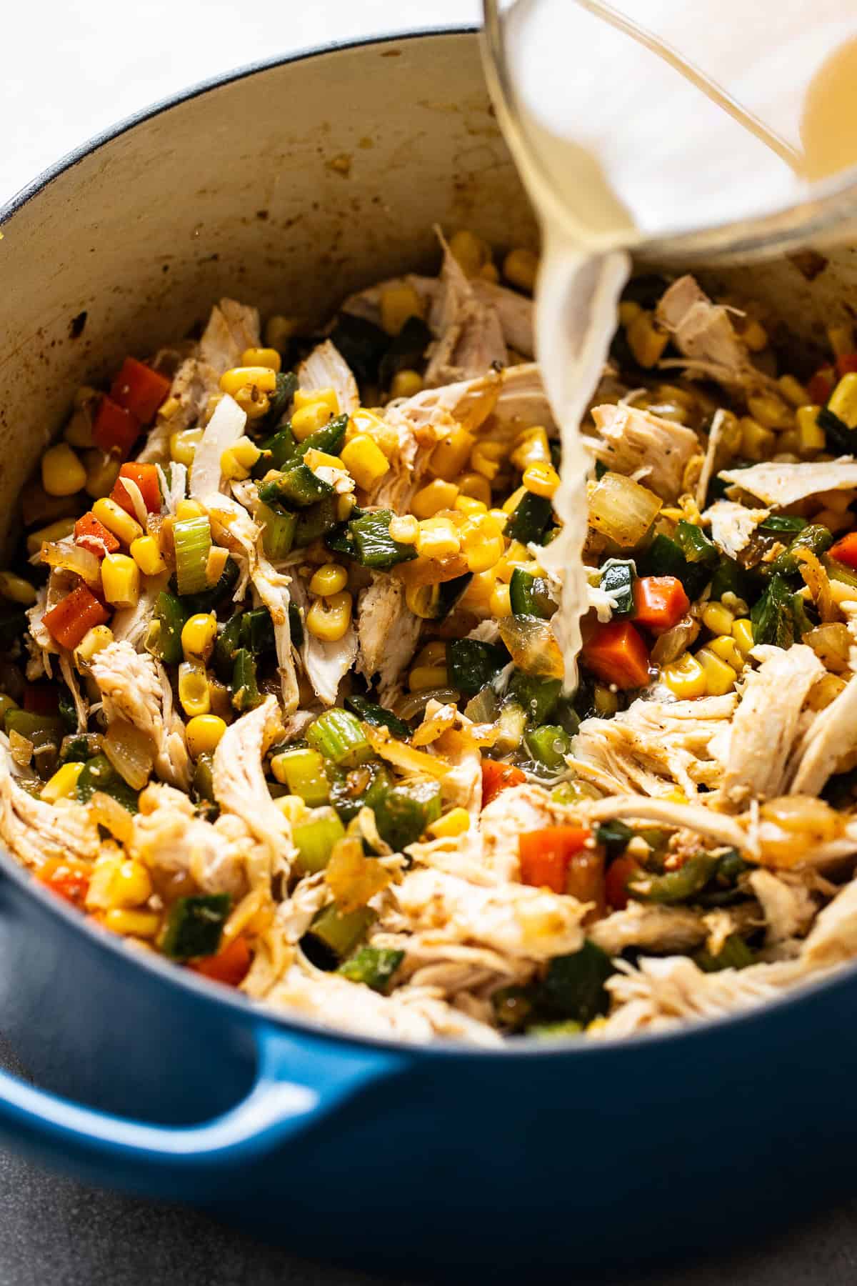 Chicken broth being poured into a pot with shredded chicken and corn.