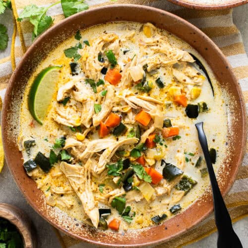 Creamy chicken poblano soup in a bowl served with fresh lime wedges, tortilla chips, and cilantro.