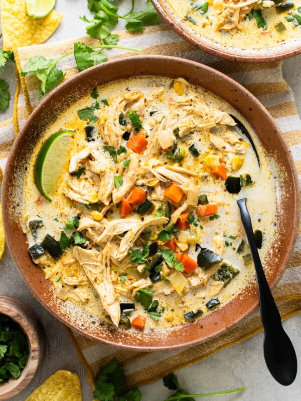 Creamy chicken poblano soup in a bowl served with fresh lime wedges, tortilla chips, and cilantro.