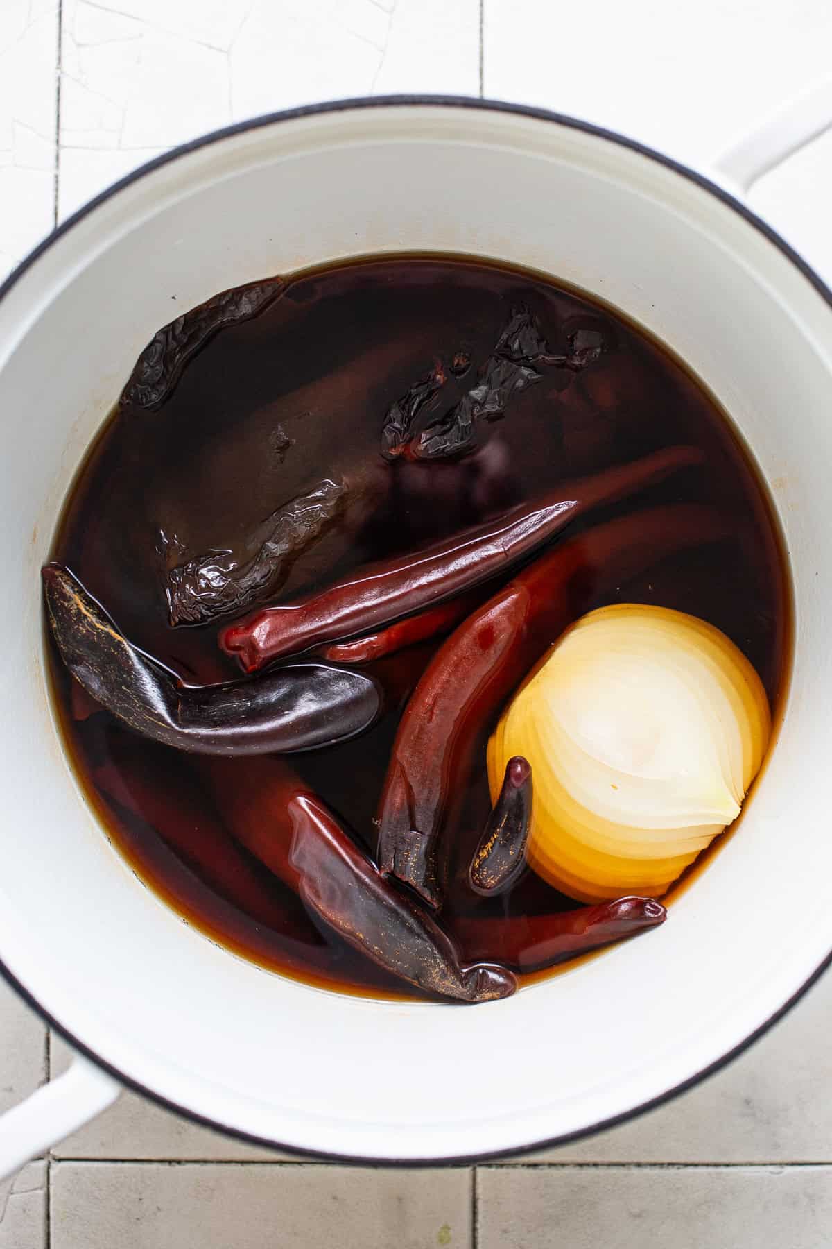 Dried Mexican chiles and an onion soaking in hot water in a pot.