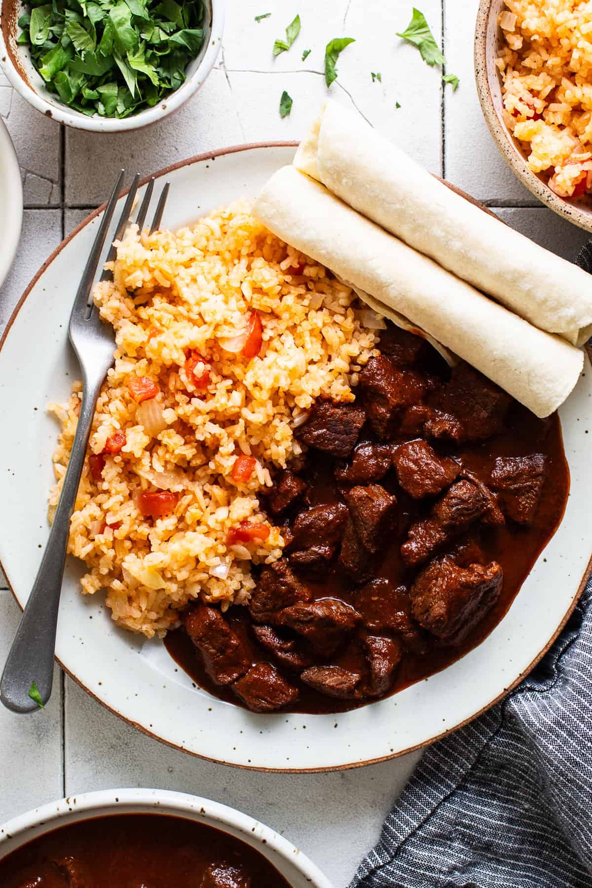 Chile colorado on a plate served with Mexican rice and corn tortillas.