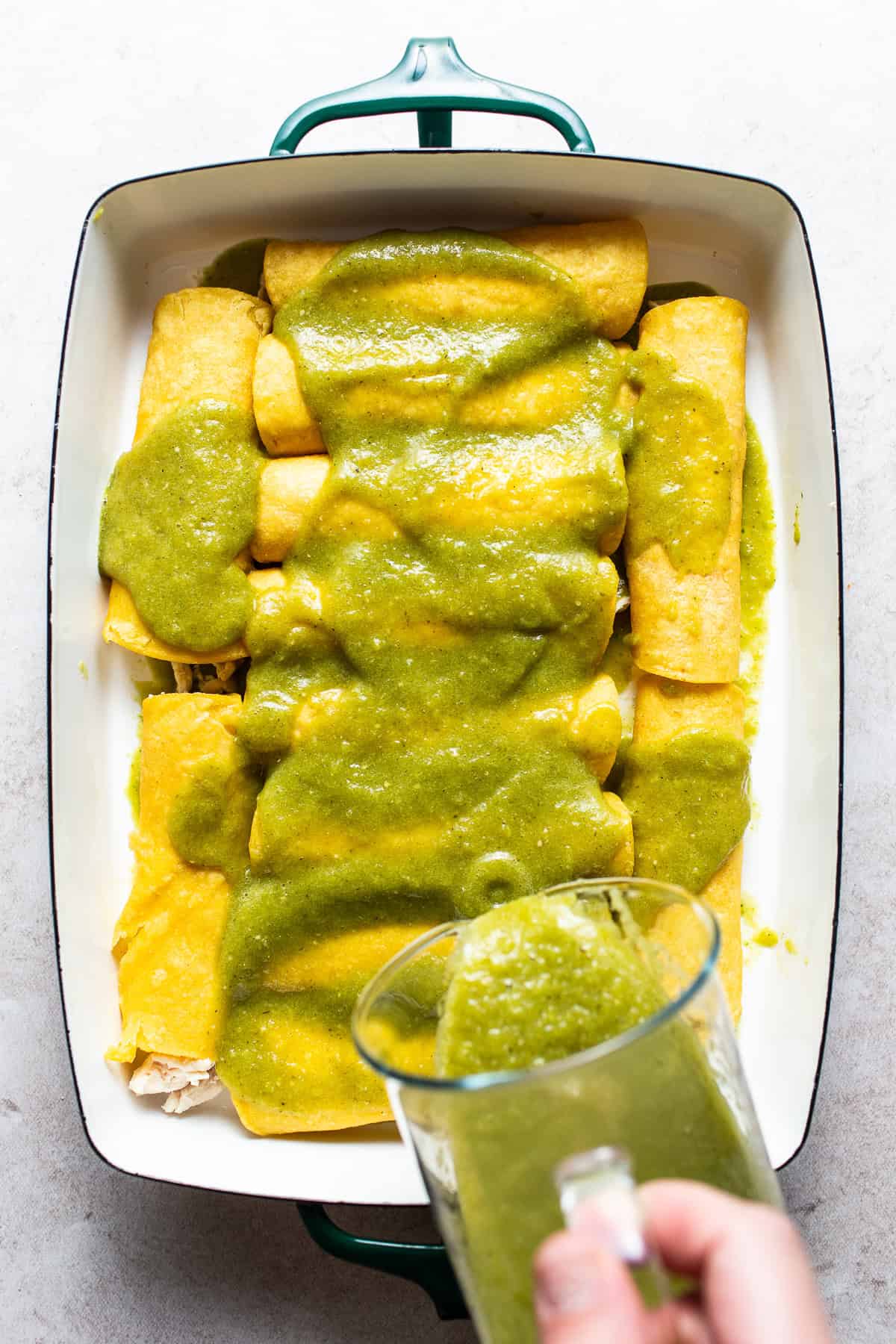 Baking dish with assembled enchiladas covered with salsa verde. 