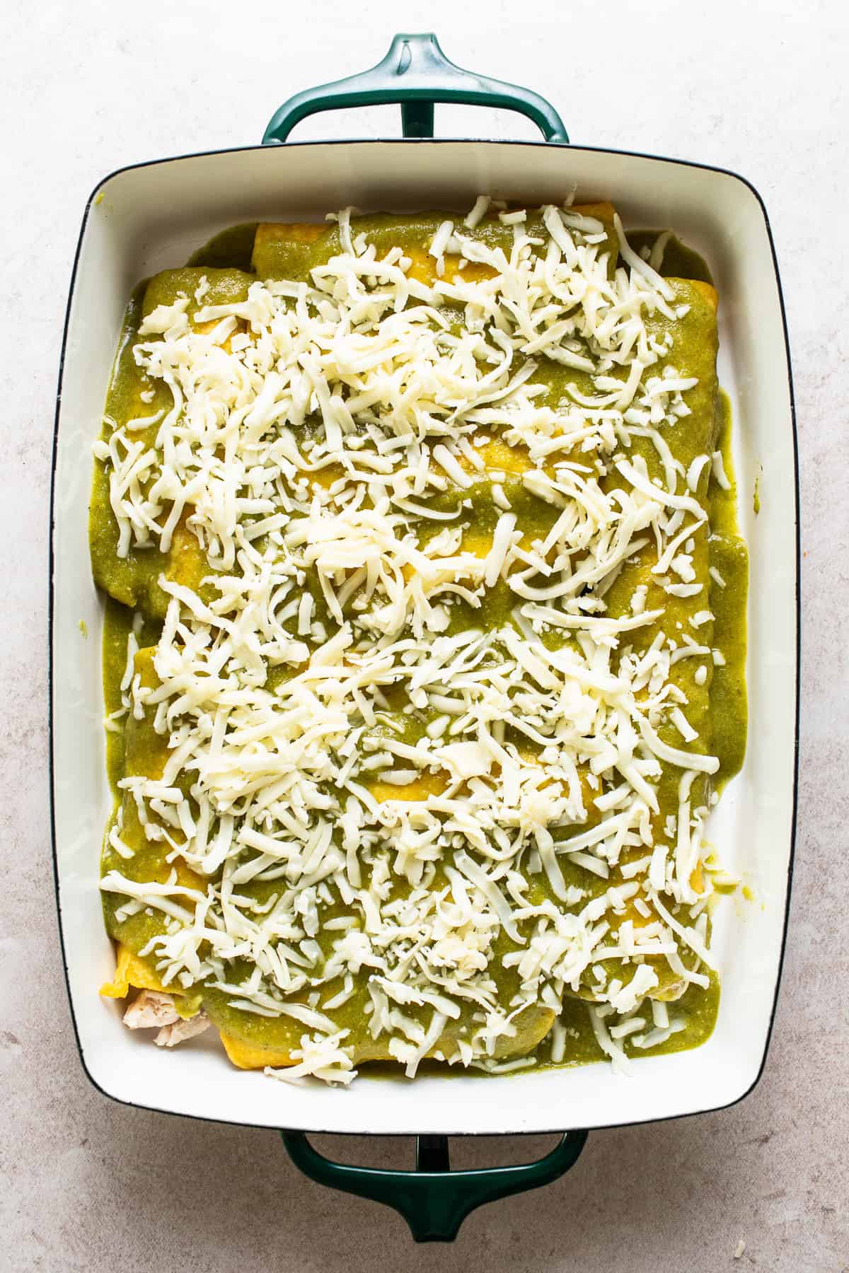 Assembled enchiladas covered with salsa verde and cheese ready to bake. 