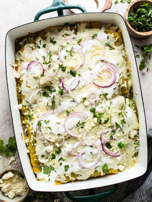 Enchiladas Verdes in a baking dish topped with cilantro, red onion, and Mexican crema or sour cream.