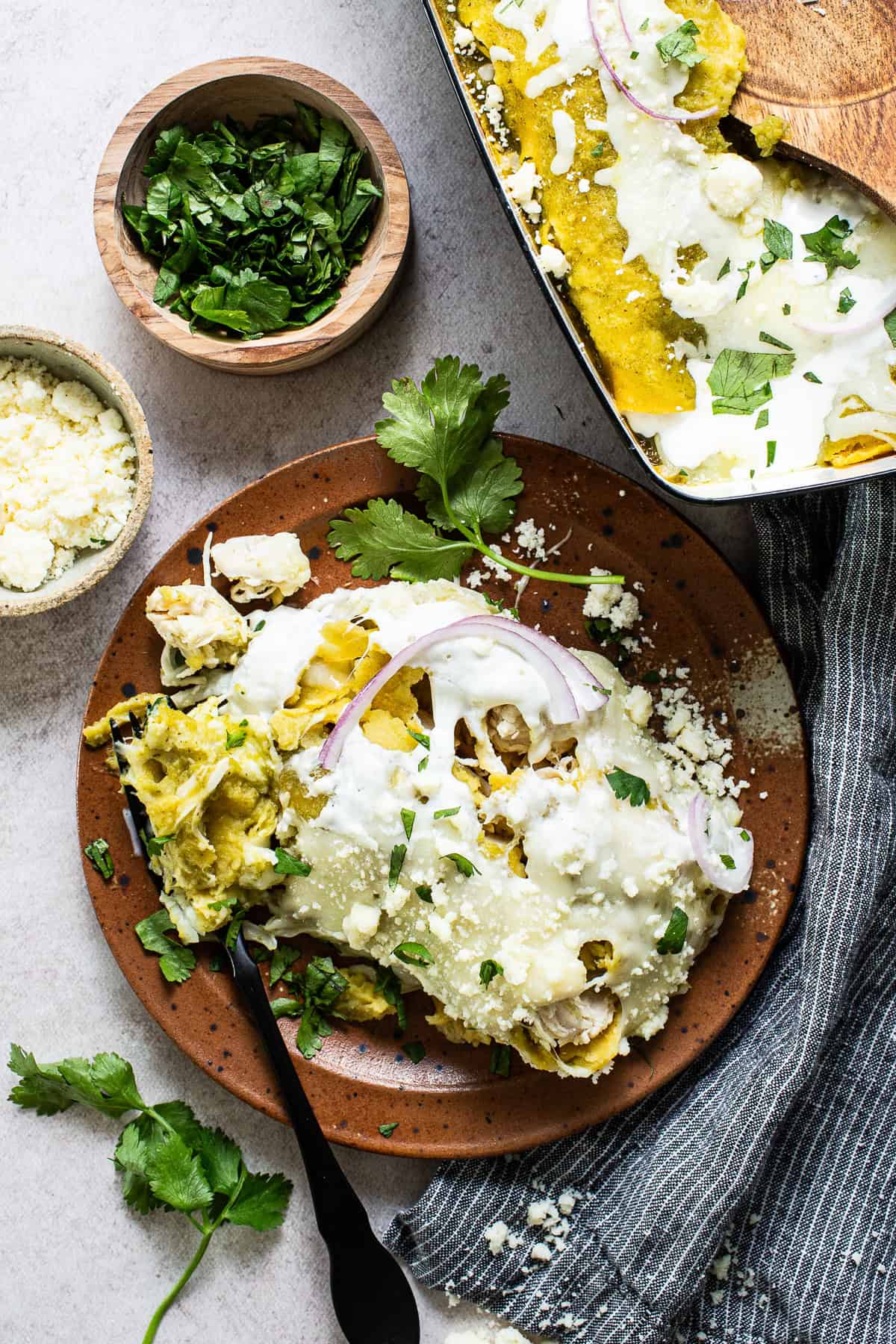 Plated enchiladas verdes topped with cilantro, onions, and Mexican crema.