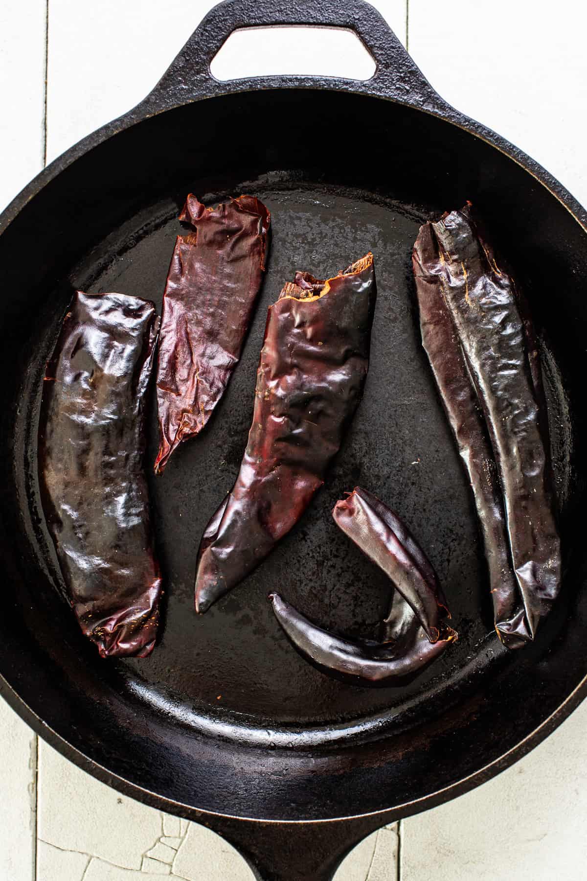 Dried guajillo chiles being toasted in a cast iron skillet.