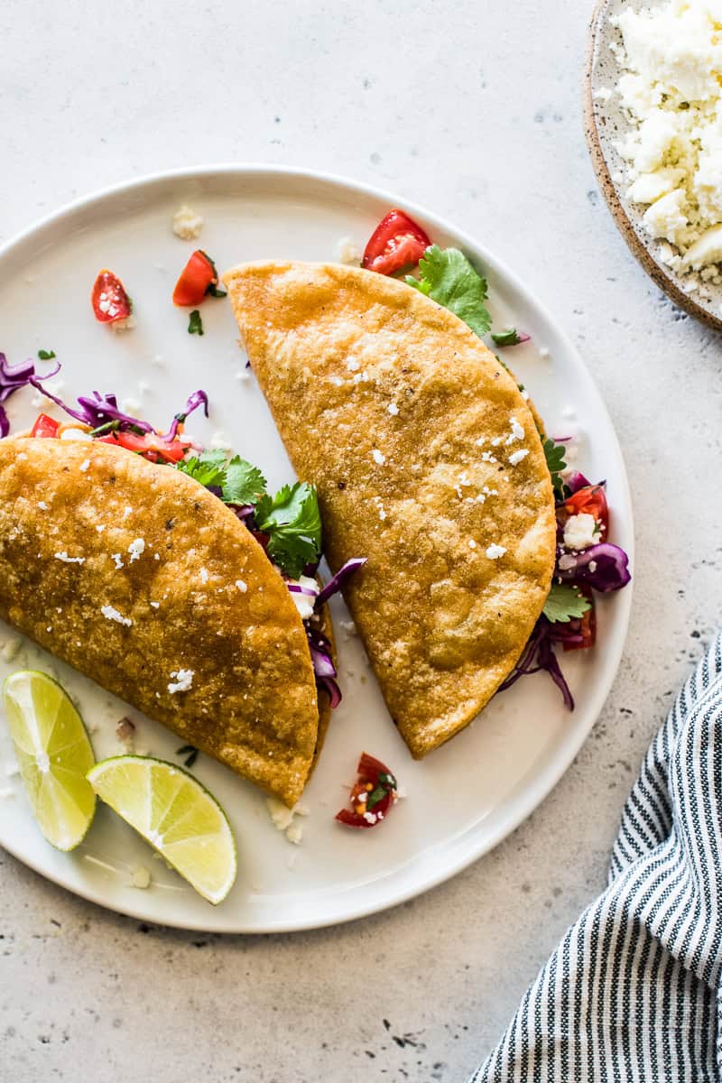 A plate of two crispy potato tacos, garnished with limes and ready to be served.