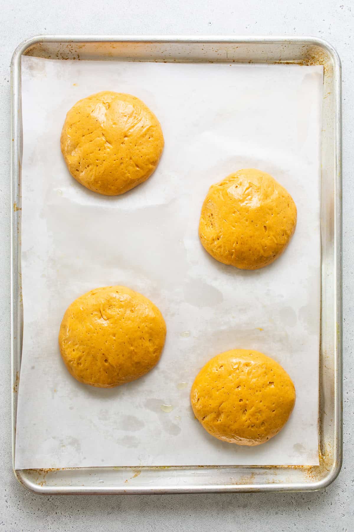 4 balls of pumpkin concha dough on a baking sheet lined with parchment paper after they've rested and risen.